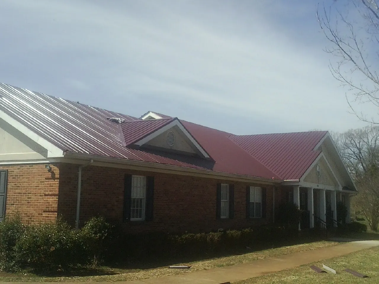 Red metal roof with gabled entries on a long brick building, from a Hail Damage Roof Repair job in Tuskegee