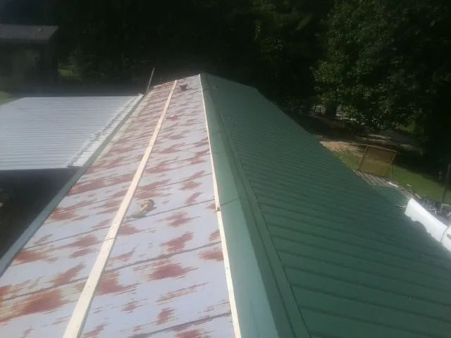 Old rusted panels beside newly installed green metal roofing — Wind Damage Roof Repair by Roofing Brothers in Tuskegee