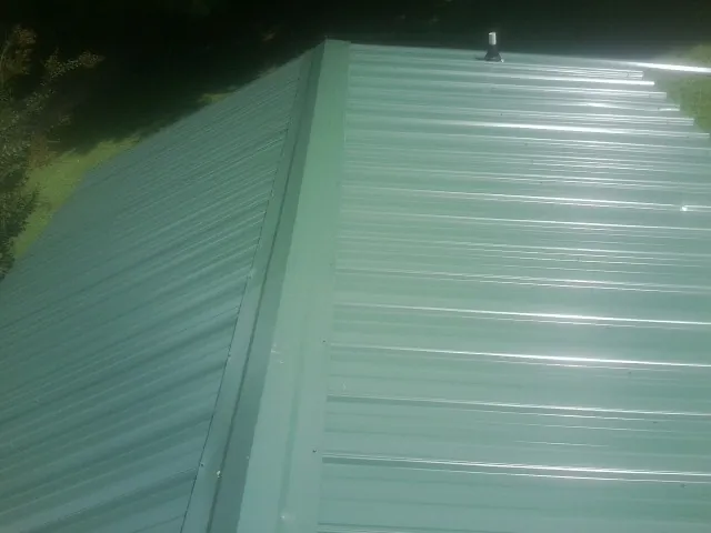 New green metal panels meeting at the ridge of a roof — Flat Roof Repair work by our crew in Tuskegee