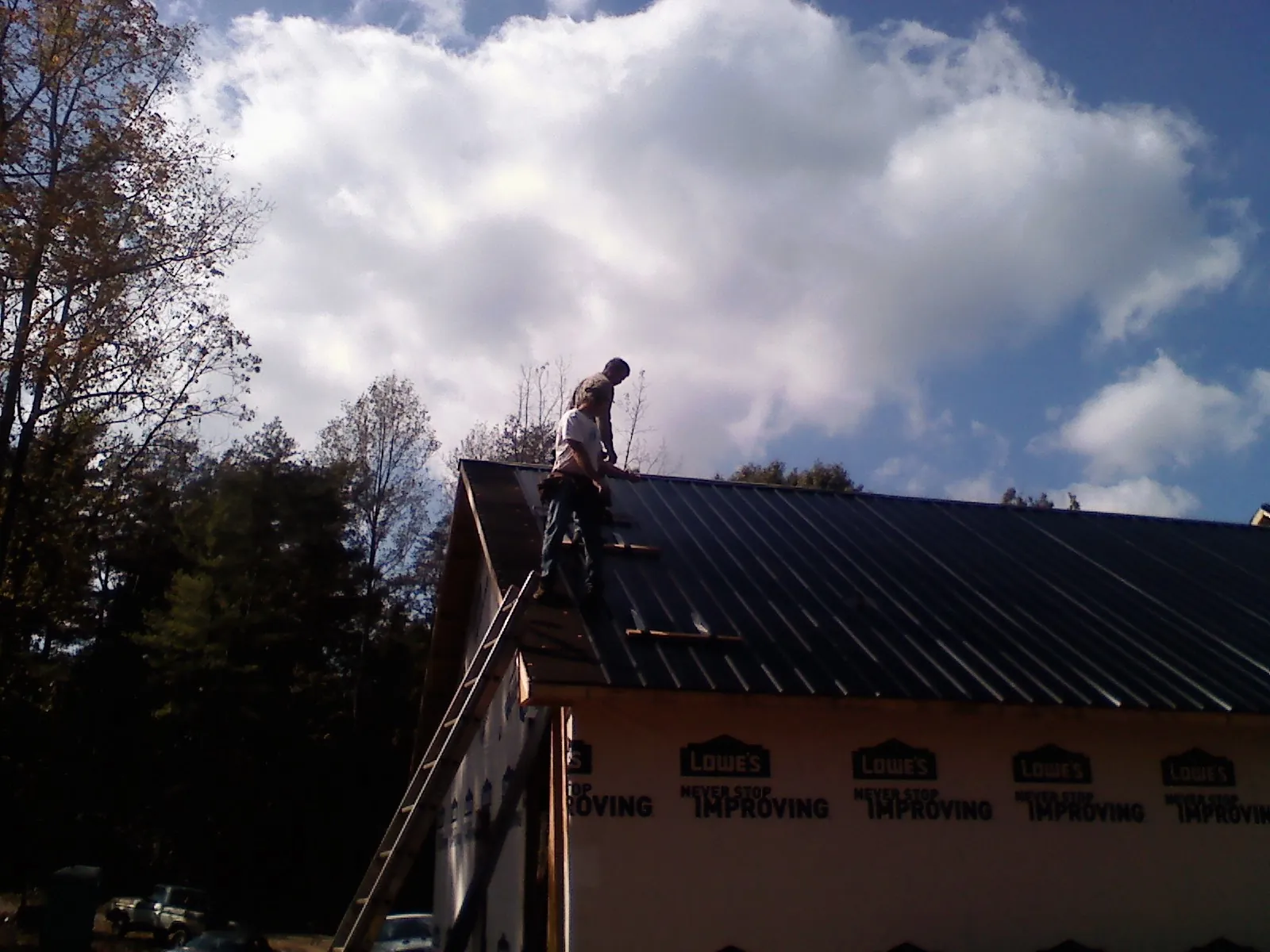 Roofer fastening dark metal panels high against a cloudy sky, from a Roof Inspection job in Tuskegee