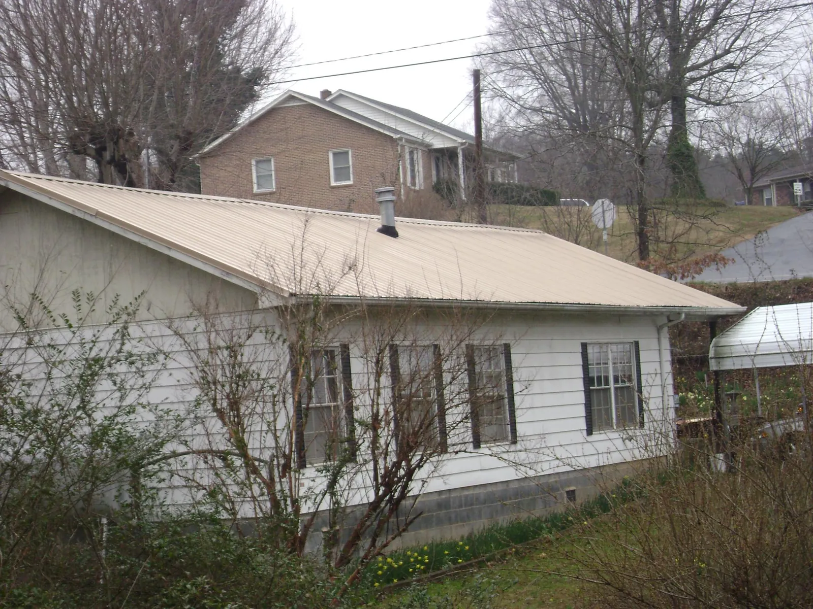 Tan metal roof on a white sided house set into a hillside — Commercial Roofing by Roofing Brothers in Tuskegee