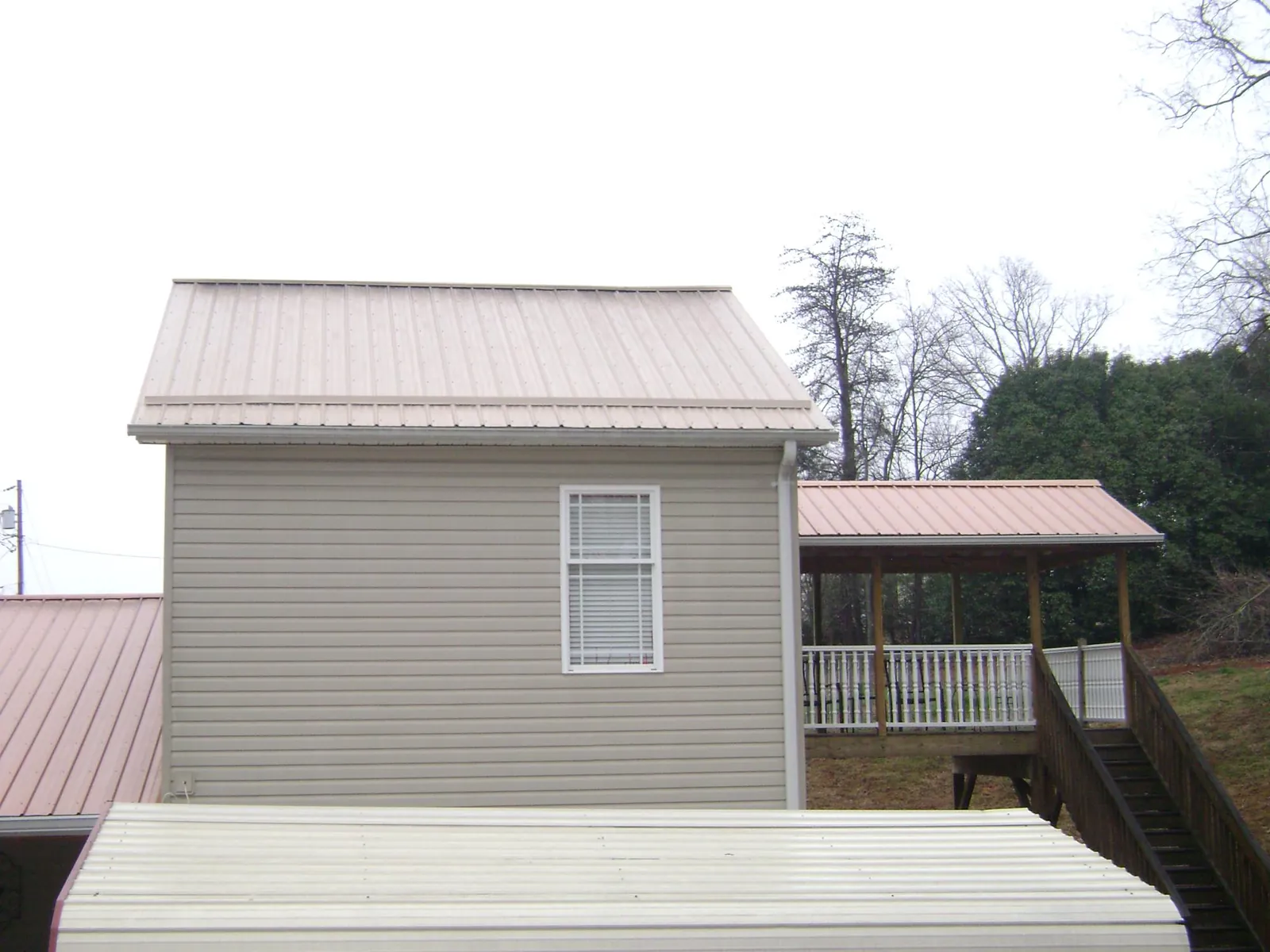 Tan metal roofs on a two story addition and attached porch, from a Roof Replacement job in Tuskegee